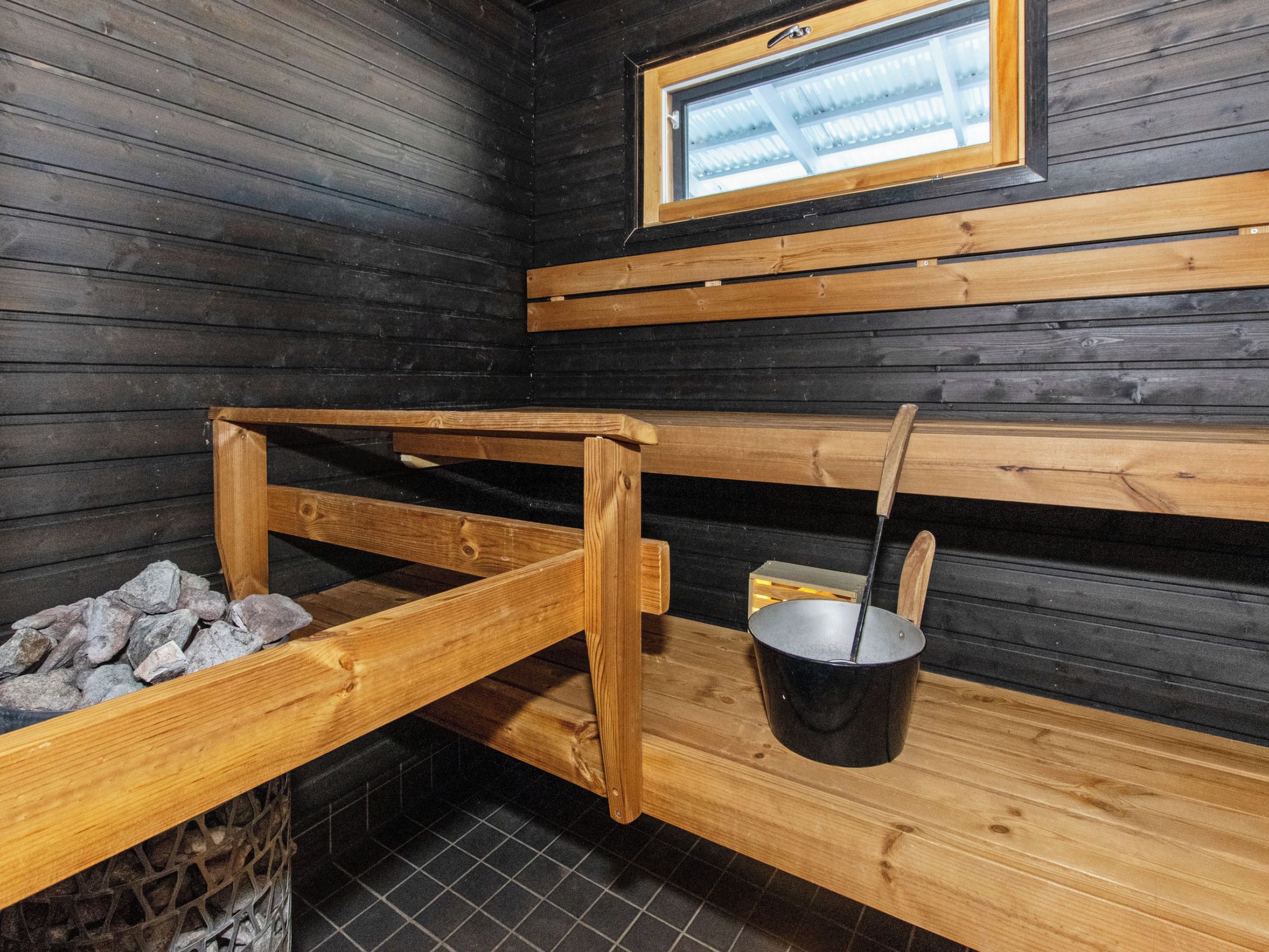 Un sauna avec des bancs en bois, un banc en pierre et un seau en métal avec une louche.