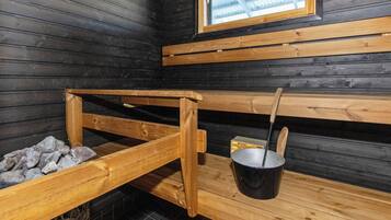 A sauna room with wooden benches, a stone bench, and a metal bucket with a ladle.