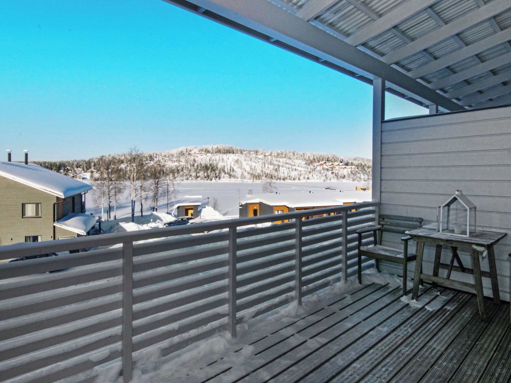 A balcony with a view of a snowy landscape, a wooden deck, and a small table with a lantern.