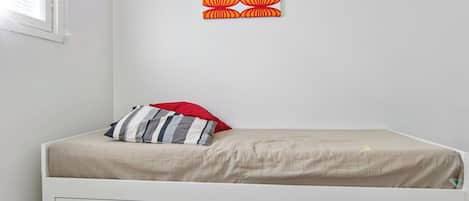 Habitación con cama individual, pared lisa, ventana y un adorno en la pared.