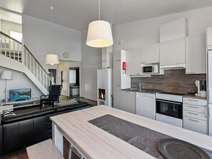 A modern kitchen with white cabinetry, a central island, a built-in stove, and a microwave. - Skivillas 78 ukkohalla (7) by Interhome (Hyrynsalmi)