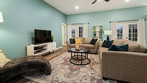A living room with a sofa, a coffee table, a TV, and a ceiling fan. - Cozy Retro Chic Sarasota Home (Sarasota)