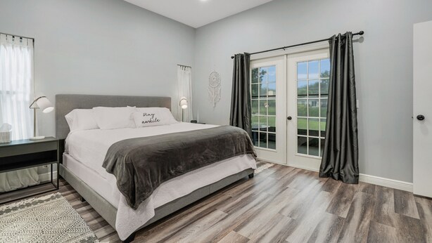 A bedroom with a bed, a ceiling fan, a nightstand, a lamp, a dreamcatcher, and a sliding glass door to the outside. - Cozy Retro Chic Sarasota Home (Sarasota)