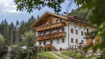 A multi-story chalet with wooden balconies, a stone pathway, and a forested backdrop.