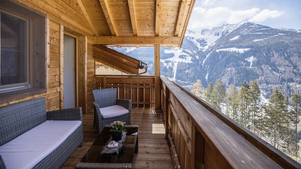 A wooden balcony with a sofa and chairs, overlooking a mountainous landscape. - Vacation Apartment "Golserhof Sonne" in the Ahrntal Valley with Mountain View (Steinhaus Ahrntal)