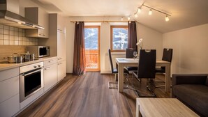 A modern kitchen with a dining area, wooden flooring, and a view of mountains through the windows. - Vacation Apartment "Golserhof Sonne" in the Ahrntal Valley with Mountain View (Steinhaus Ahrntal)