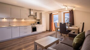 A modern kitchen with white cabinets, a dining area with a table and chairs, and a sofa with a green pillow. - Vacation Apartment "Golserhof Sonne" in the Ahrntal Valley with Mountain View (Steinhaus Ahrntal)