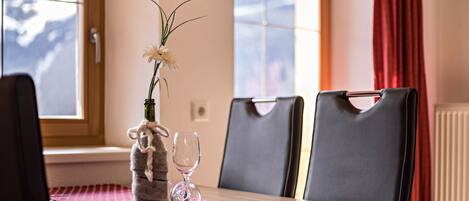 A dining table with a red tablecloth, two chairs, a vase with a plant, and a wine glass.