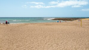 A sandy beach with a clear sky, a few people, and a distant kite.