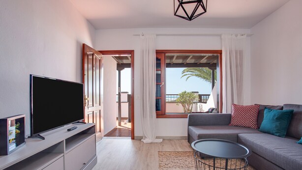 A modern living room with a flat-screen TV, a sofa, a coffee table, and a balcony with a view.