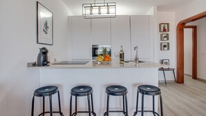 A modern kitchen with a central island, bar stools, a coffee machine, and a hanging light fixture.