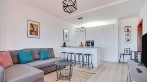 A modern living room with a grey sofa, a round coffee table, and a kitchen area with bar stools.