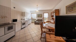 Una cocina con armarios blancos, una mesa de comedor con sillas, un televisor y un cuadro en la pared.
