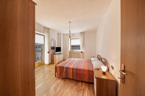 Une chambre avec un lit en bois, une table de chevet avec une lampe, une fenêtre avec des rideaux et une vue sur un balcon.