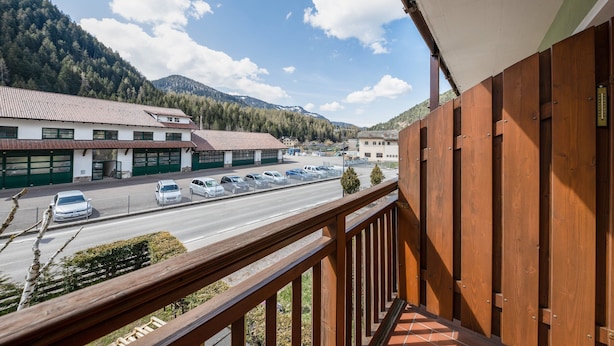 Un balcón con vista a una calle, un estacionamiento y una cordillera.