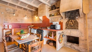 Une cuisine rustique aux murs de pierre, avec une table en bois, des chaises, un four à micro-ondes, une cuisinière et un four à bois.