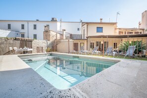 Une piscine avec des chaises longues, un mur en pierre et, au fond, un bâtiment doté d’un toit en tuiles.