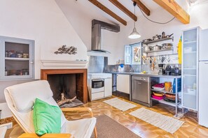 A modern kitchen with a fireplace, wooden beams, and a dining area with a white chair and green pillow.