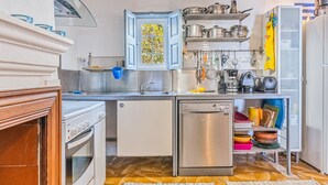 Una cocina compacta con horno integrado, lavavajillas y ventana con contraventanas azules.