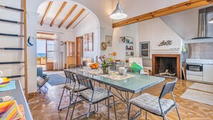 Una cocina amplia con un horno moderno, un comedor con mesa de vidrio y sillas de metal, y techo de madera.