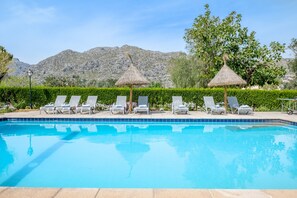 A swimming pool with lounge chairs and thatched umbrellas, surrounded by greenery and mountains. - Roomy Villa “Villa Agnes” with Mountain View, Pool, Terrace & Garden (Pollensa)