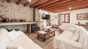 A cozy living room with a stone wall, wooden beams, a fireplace, a television, and a sofa. - Roomy Villa “Villa Agnes” with Mountain View, Pool, Terrace & Garden (Pollensa)