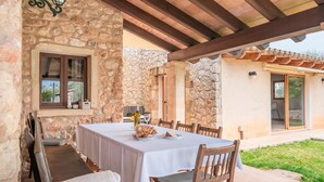 A stone building with a covered patio, a table set for dining, and a view of the surrounding landscape. - Roomy Villa “Villa Agnes” with Mountain View, Pool, Terrace & Garden (Pollensa)