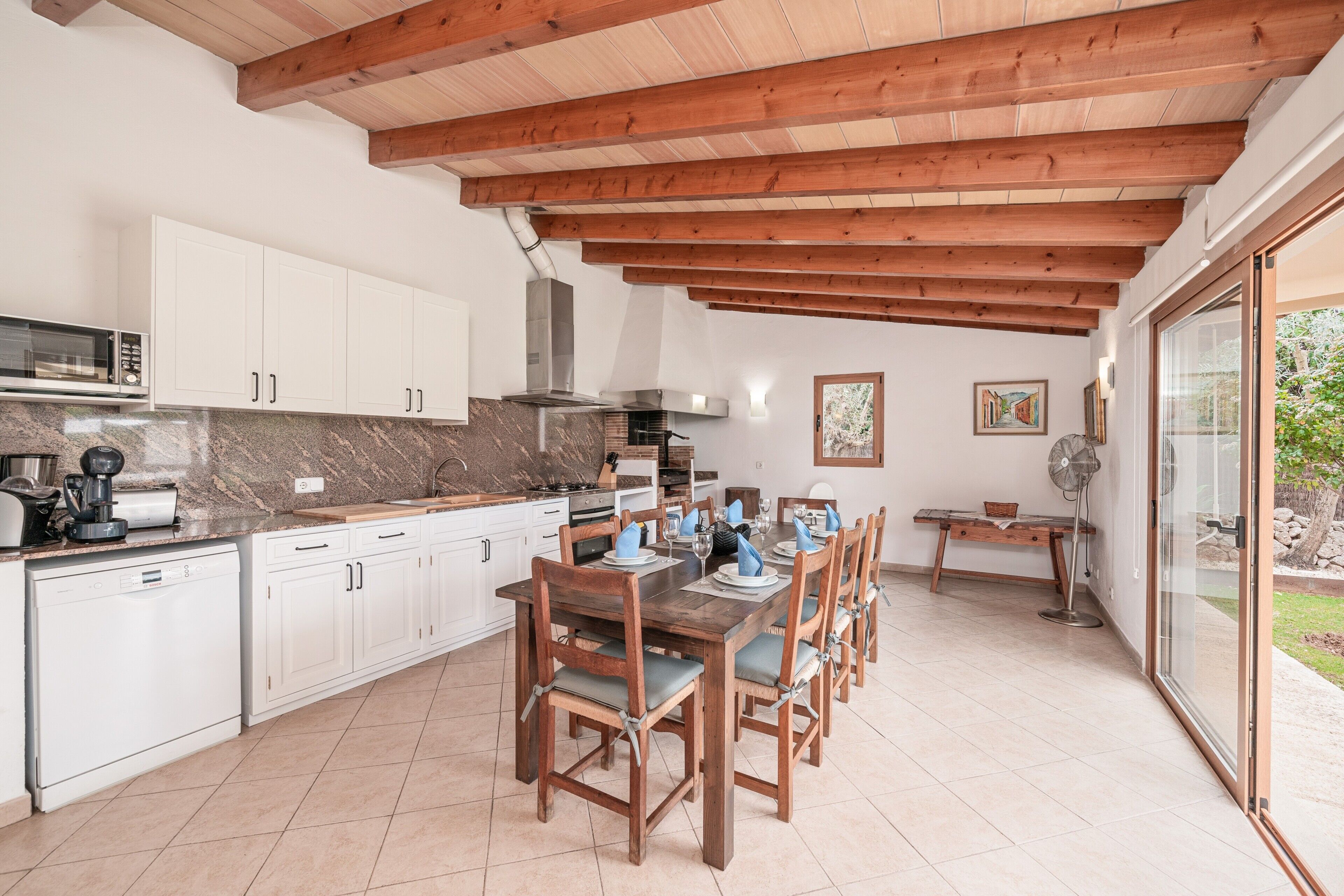 A kitchen with wooden beams, white cabinets, and a dining area with a table and chairs.