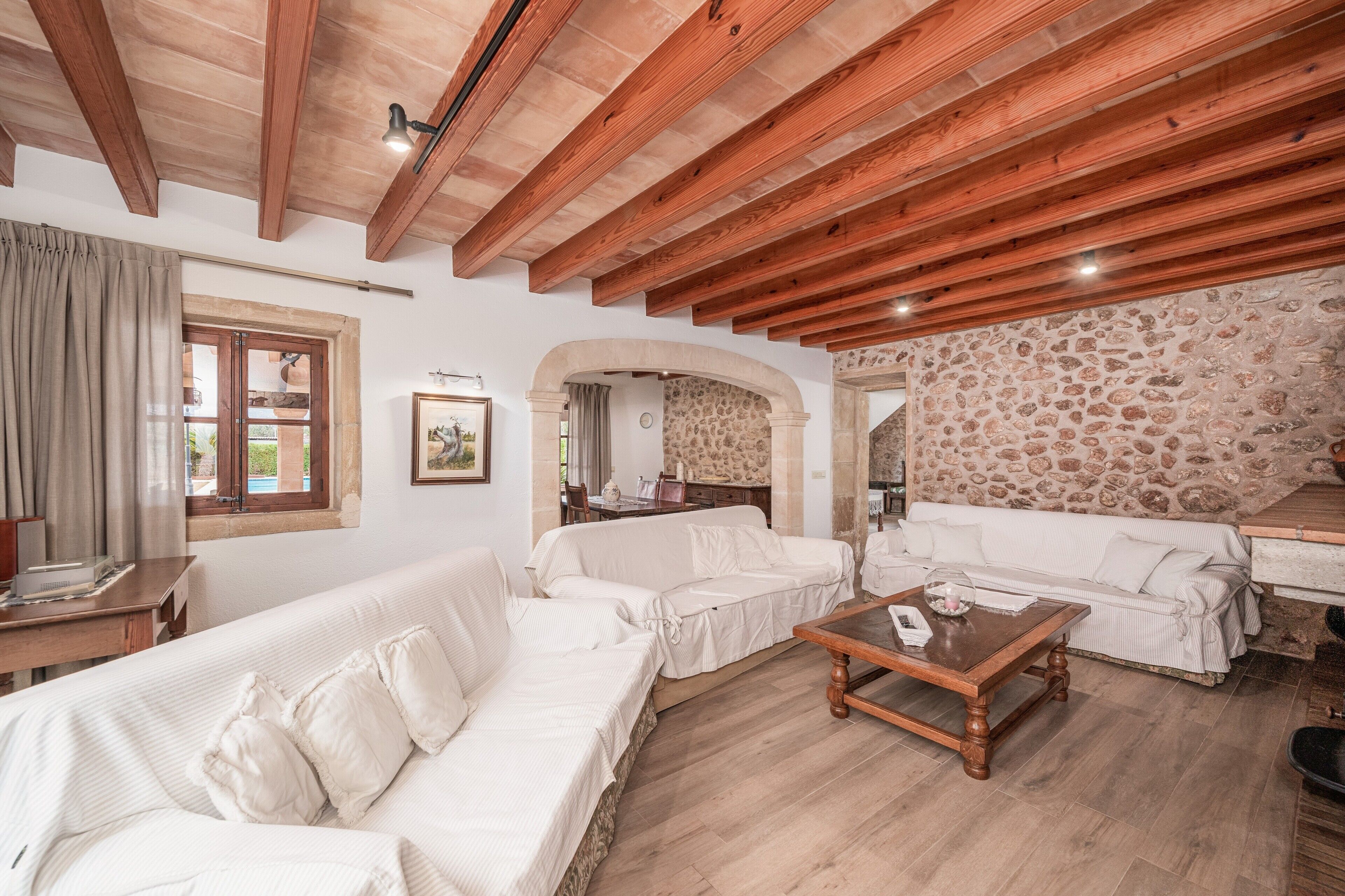 Amplia sala de estar con vigas de madera, pared de piedra y sofá blanco.