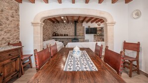 A dining room with a wooden table, chairs, and a stone wall. - Roomy Villa “Villa Agnes” with Mountain View, Pool, Terrace & Garden (Pollensa)