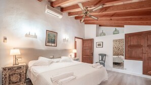 A bedroom with a bed, bedside lamps, a ceiling fan, wooden beams, a mirror, and a small table with a chair. - Roomy Villa “Villa Agnes” with Mountain View, Pool, Terrace & Garden (Pollensa)