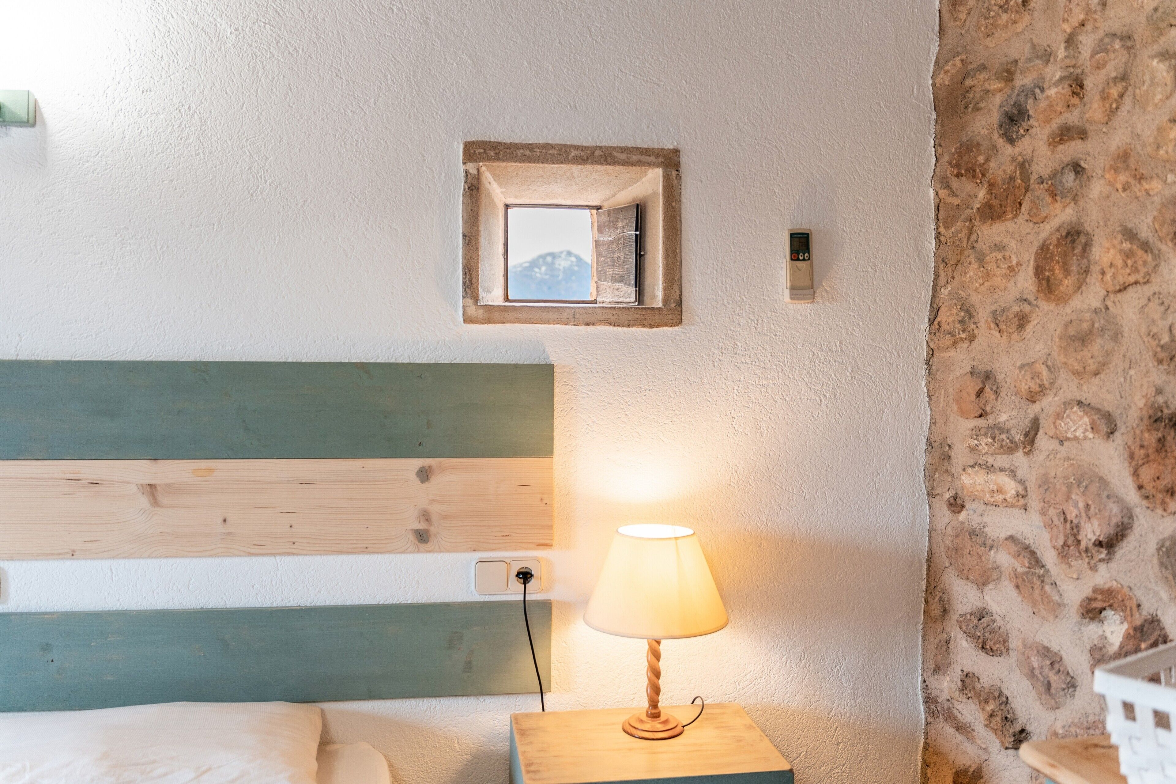 Une chambre à coucher avec une tête de lit en bois, une lampe de chevet, un petit miroir et un mur en pierre.