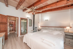 Une chambre avec un grand lit, des poutres apparentes en bois au plafond, un ventilateur de plafond et une table de chevet avec une lampe.