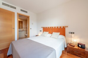 A bedroom with a large bed, wooden wardrobe, bedside table, and a nightstand with a lamp.