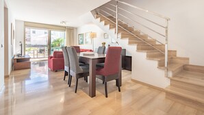 A spacious dining area with a wooden staircase, modern furniture, and a view to the outside.
