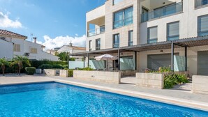A modern poolside area with a clear blue pool, a covered seating area, and a multi-story building with balconies.