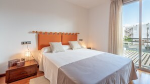 A bedroom with a bed, bedside tables, a nightstand, a window with a view of buildings, and a curtain.