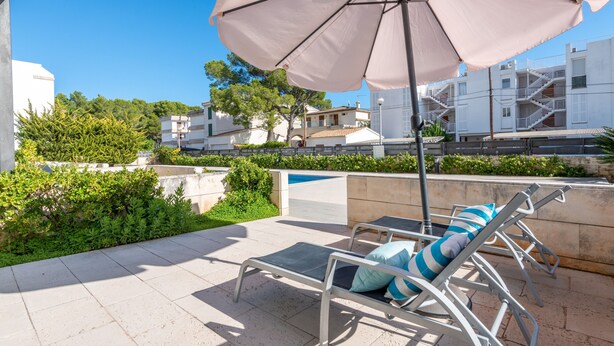 A rooftop terrace with lounge chairs, a large umbrella, and a pool in the background.