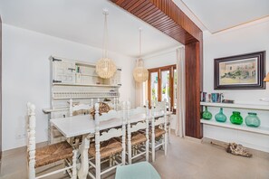 Een eetruimte met een witte tafel en stoelen, hangende rieten kroonluchters en een houten plafond.