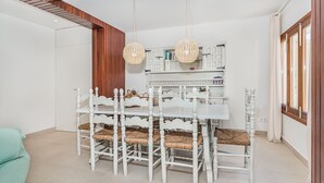 A dining area with a white table and chairs, a wooden ceiling, and a white cabinet with books. - In perfect location to beach and city - Villa Hibiscus (Pollensa)