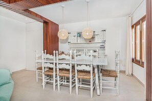 Een eetruimte met een witte tafel en stoelen, een houten plafond en een witte kast met boeken.