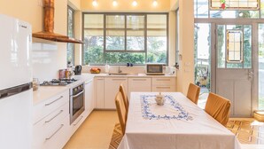 A modern kitchen with white cabinets, a stove, and a dining area with a table set for two. - Unique Country House In Central Israel (Hefer Valley)