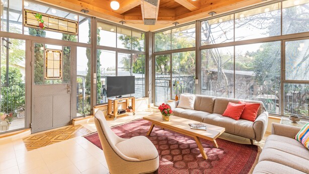 A spacious living room with a large sofa, a coffee table, and a TV. The room has large windows and wooden beams on the ceiling. - Unique Country House In Central Israel (Hefer Valley)