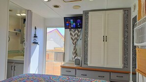 Un dormitorio con una cama grande, un armario, un televisor montado en la pared y una ventana con vistas a un edificio.