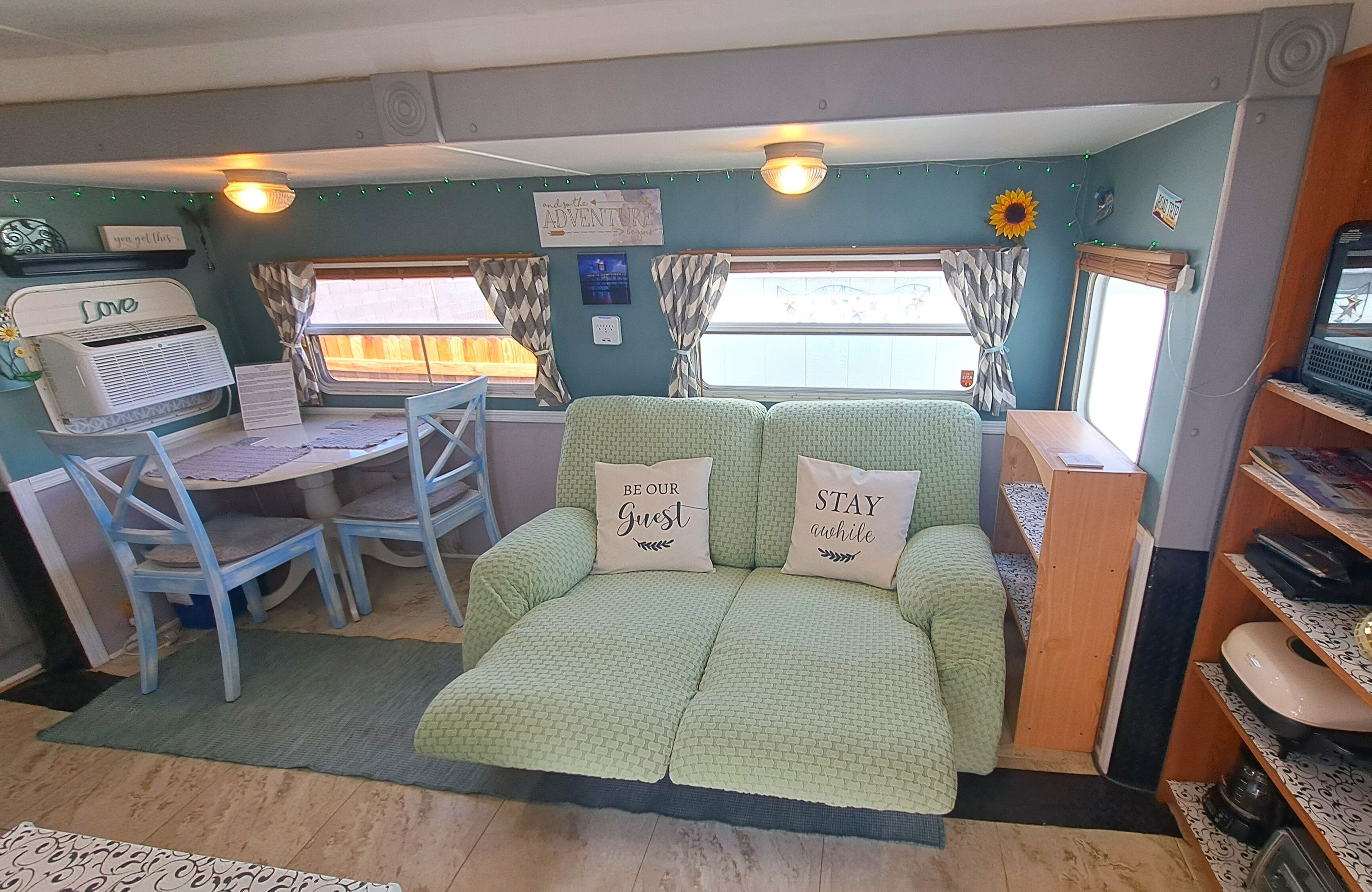 A cozy RV interior with a green couch, a small desk, and a television.