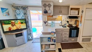 A compact kitchen with a TV, cabinets, and a microwave. - Foothills Quiet Guest RV Home - Queen, Twin, Dogs + Fenced, BBQ, Laundry Service (Yuma)