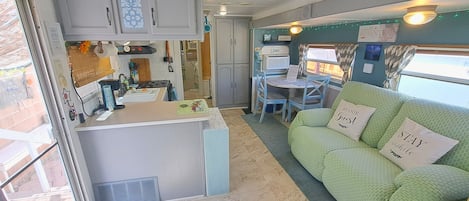 A compact RV interior with a kitchenette, a dining area, and a green couch with guest pillows.