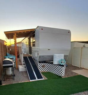 A mobile home with a covered patio area, a ramp leading to the entrance, and a small outdoor seating area.