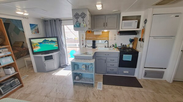 A compact kitchen with a TV, a sink, a stove, and a refrigerator.