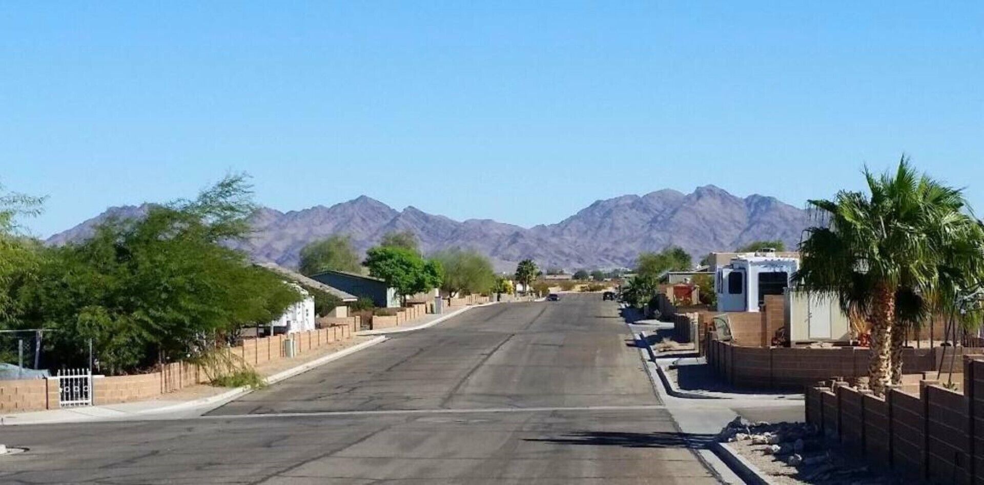 Una calle flanqueada por casas, cielo despejado y montañas al fondo.